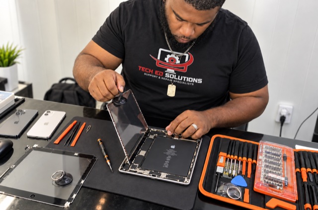 A TechEd and Solutions technician lifting the screen off an iPad with a suction tool at the repair bench