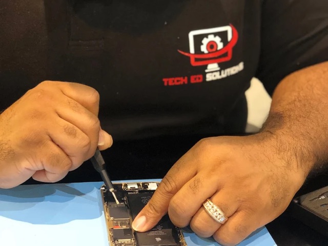 A TechEd and Solutions technician in a branded polo shirt working on an opened iPhone with a screwdriver